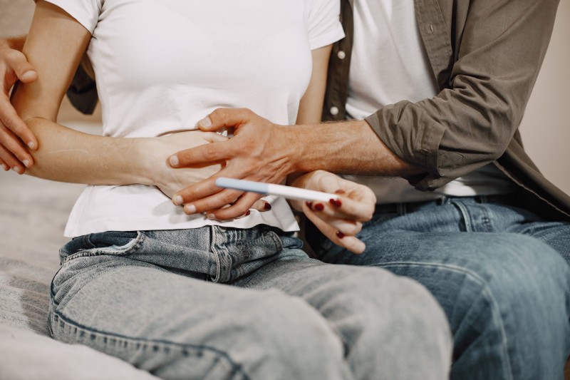 Couple sitting together at home, gently holding hands and looking at a pregnancy test.