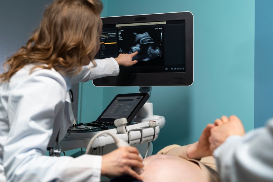Gynecologist performing an ultrasound examination on a pregnant patient while viewing a fetal image on the monitor.