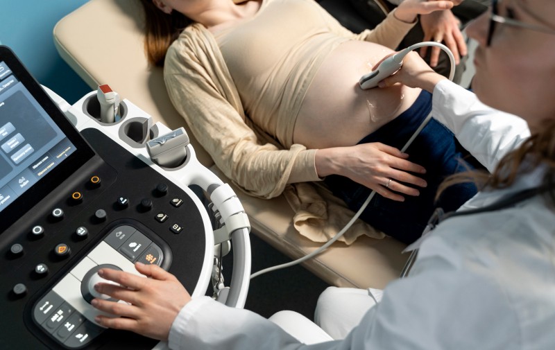 Pregnant woman receiving an abdominal ultrasound examination from a healthcare professional.