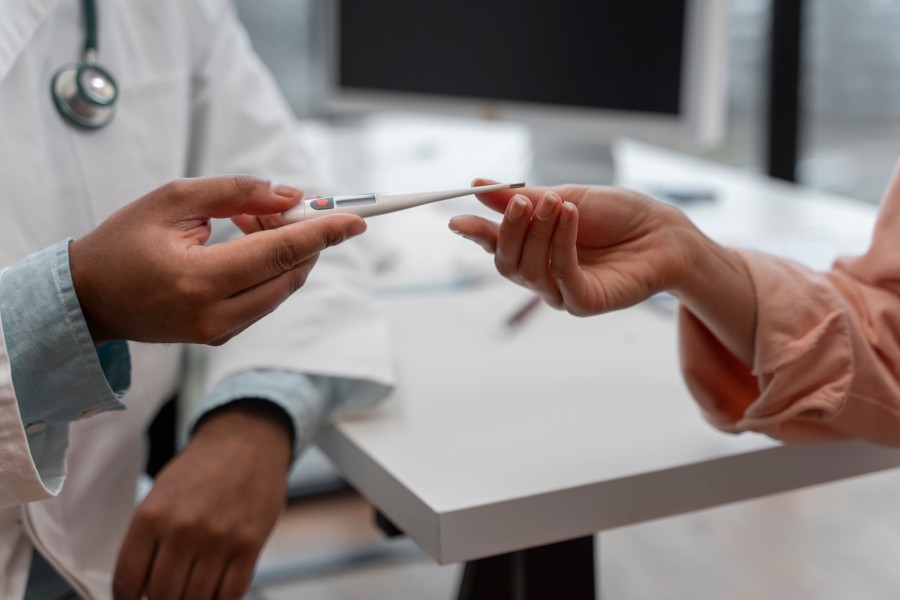 Doctor handing a digital thermometer to a female patient during a medical consultation for health assessment.