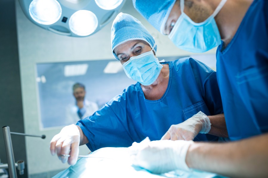 Surgeons in blue scrubs, masks, and caps performing an operation in a hospital operating room