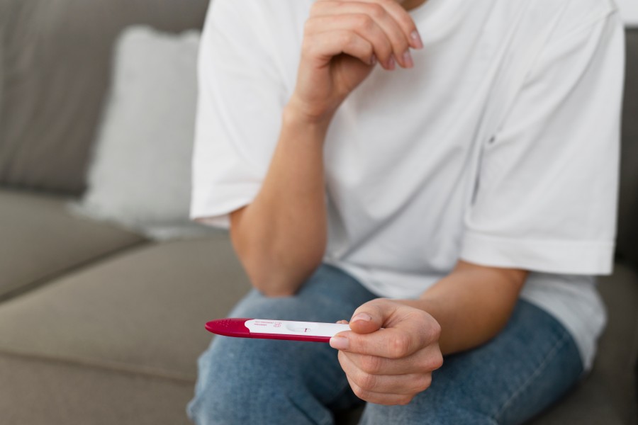 Woman holding a positive pregnancy test while sitting on a couch